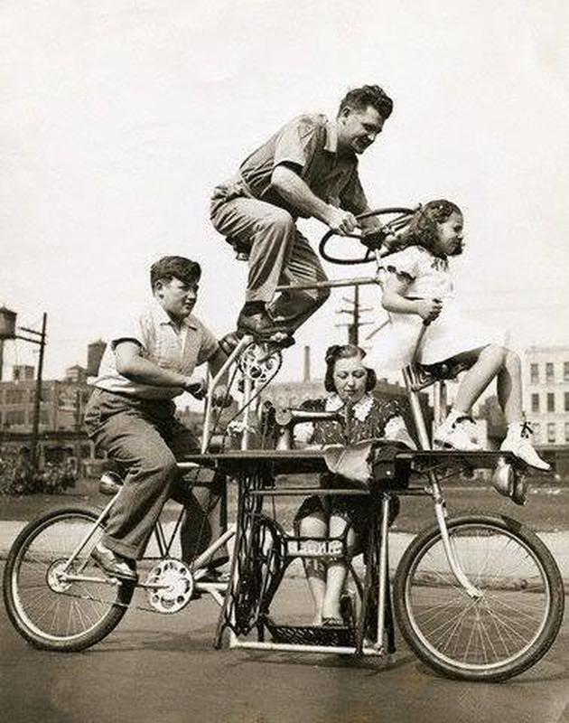 A vintage black-and-white photo shows four people riding a unique, multi-level bicycle with a sewing machine built in. One woman sits and sews, while two men and a girl pedal and balance on different parts of the bike.