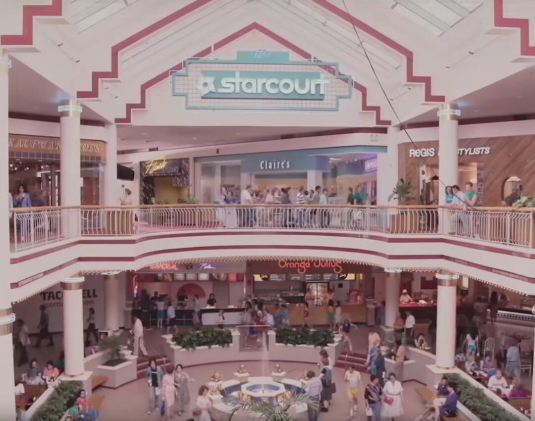 A busy two-level shopping mall with a large "Starcourt" sign, multiple stores including Claire’s, and people walking, sitting, and shopping around a central fountain area.