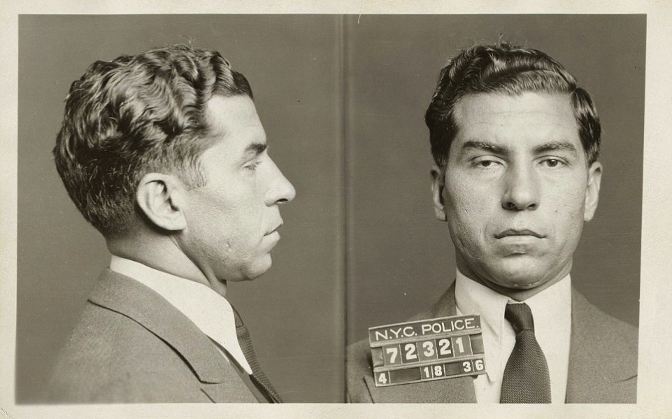 Black-and-white mugshot showing a man in a suit and tie, photographed from the side and front. He holds a placard that reads “N.Y.C. POLICE 72321 4/18/36.”