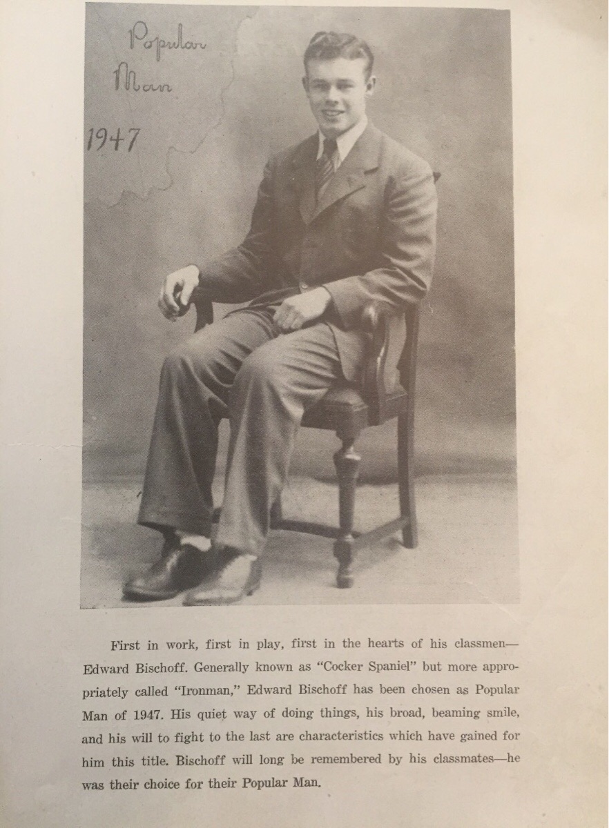A sepia-toned photo of a young man in a suit sitting on a chair, smiling. Handwritten text above reads “Popular Man 1947.” A printed caption below describes his achievements and title as Popular Man of 1947.