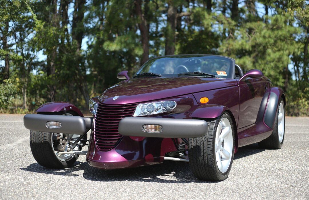 A purple Plymouth Prowler convertible is parked on a paved surface with trees in the background on a sunny day.