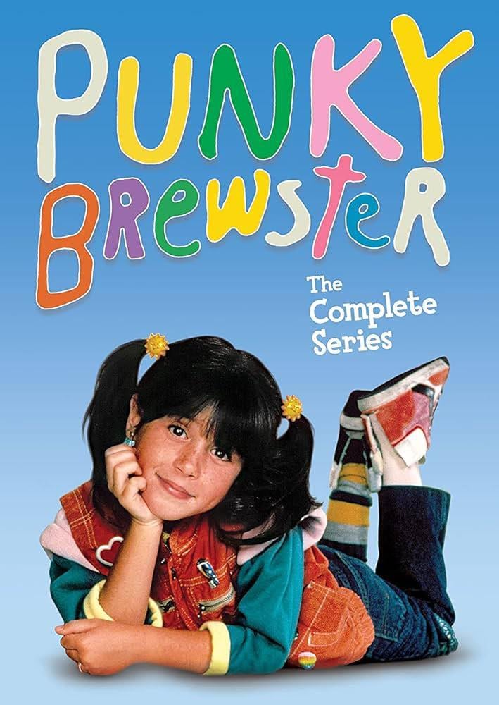 A young girl with dark pigtails, colorful clothes, and sneakers lies on her stomach, smiling. Above her, colorful text reads "Punky Brewster," and white text says "The Complete Series" on a blue background.