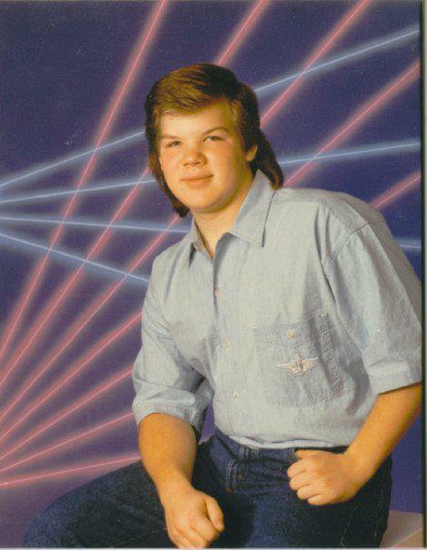 A young person with medium-length brown hair sits, wearing a light blue button-up shirt and jeans. The background features pink and blue laser beams on a purple backdrop, creating a retro 1980s vibe.