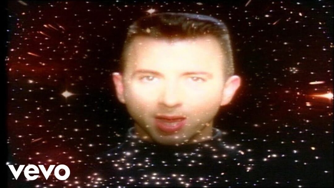 A person’s face is centered against a star-filled, cosmic background. The individual appears to be floating in space, with bright light reflecting on their face. The word "vevo" is in the bottom left corner.