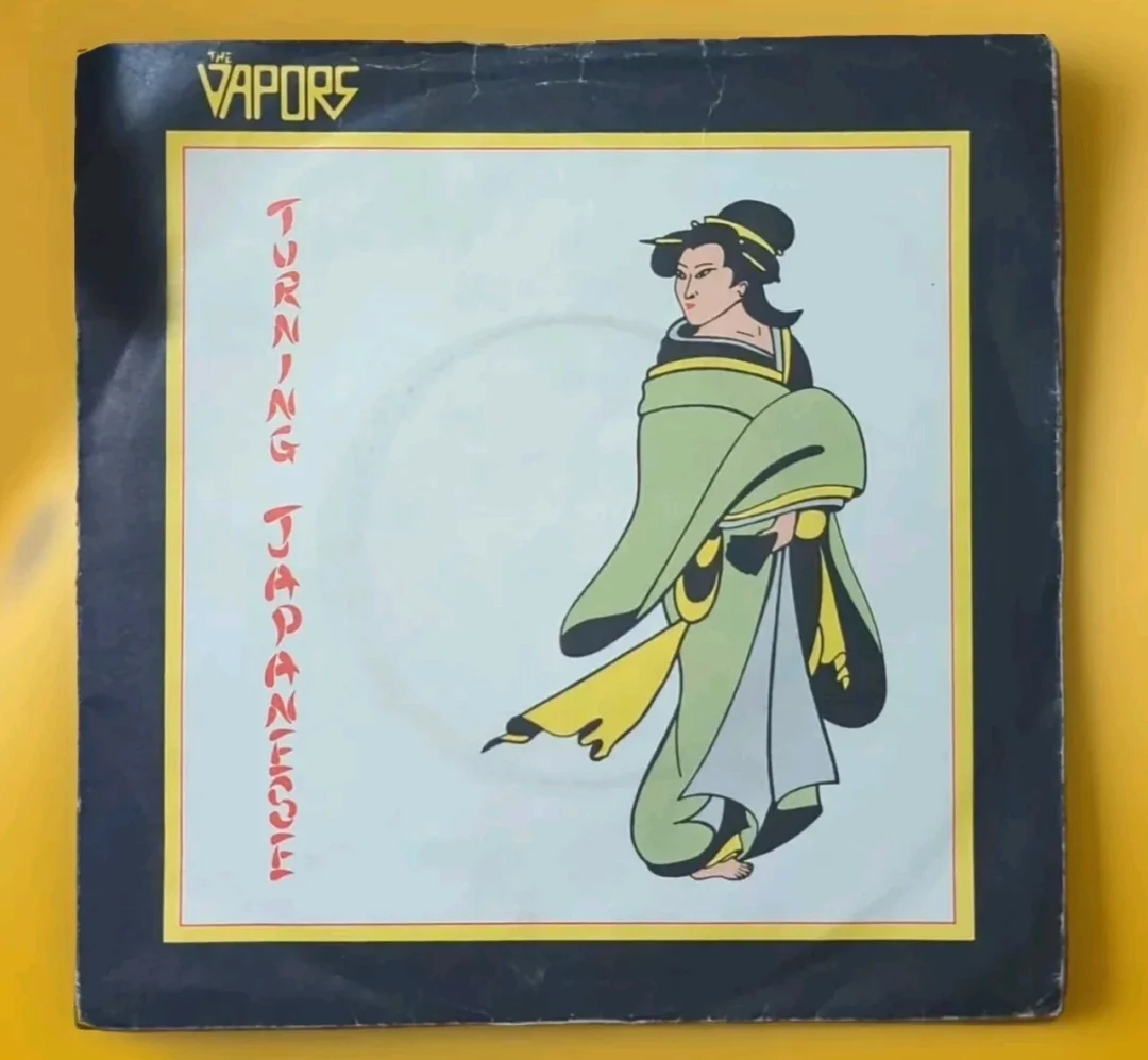 Album cover for "Turning Japanese" by The Vapors, featuring stylized text and an illustration of a person in traditional Japanese attire on a black and yellow background.