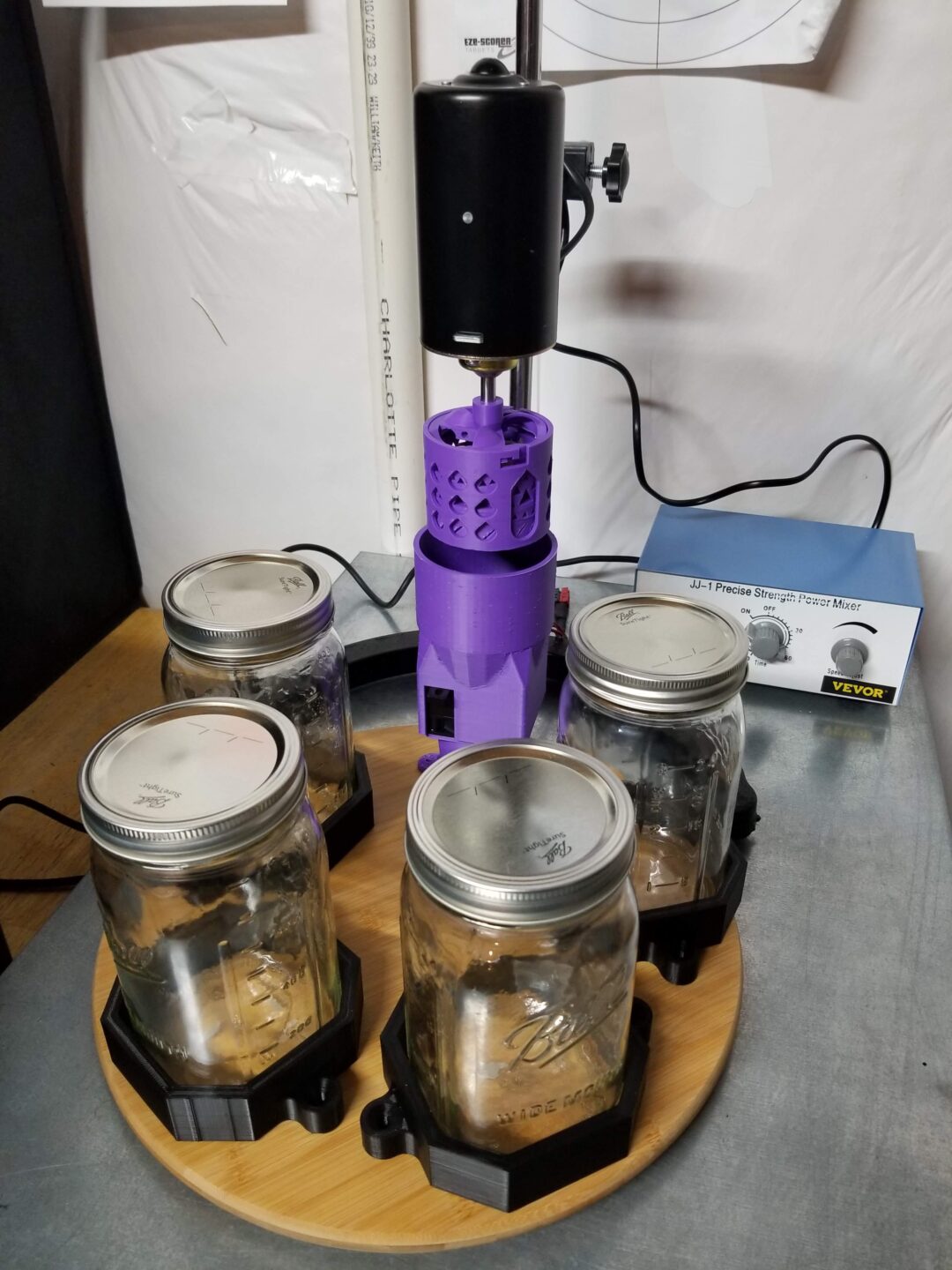 A laboratory device with four mason jars held in black holders on a round wooden platform, connected to a central black and purple motorized apparatus, with a control box labeled "VEVOR" in the background.