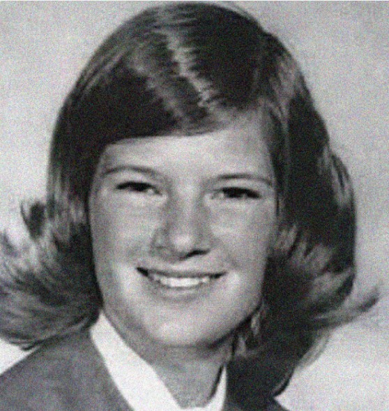 A black and white portrait of a young person with shoulder-length hair, wearing a collared shirt and smiling at the camera.