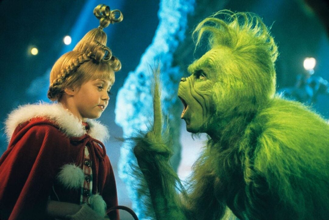 A young girl in a red cape with ornate hair stands facing a furry green creature with a surprised expression in a fantastical, snowy setting.