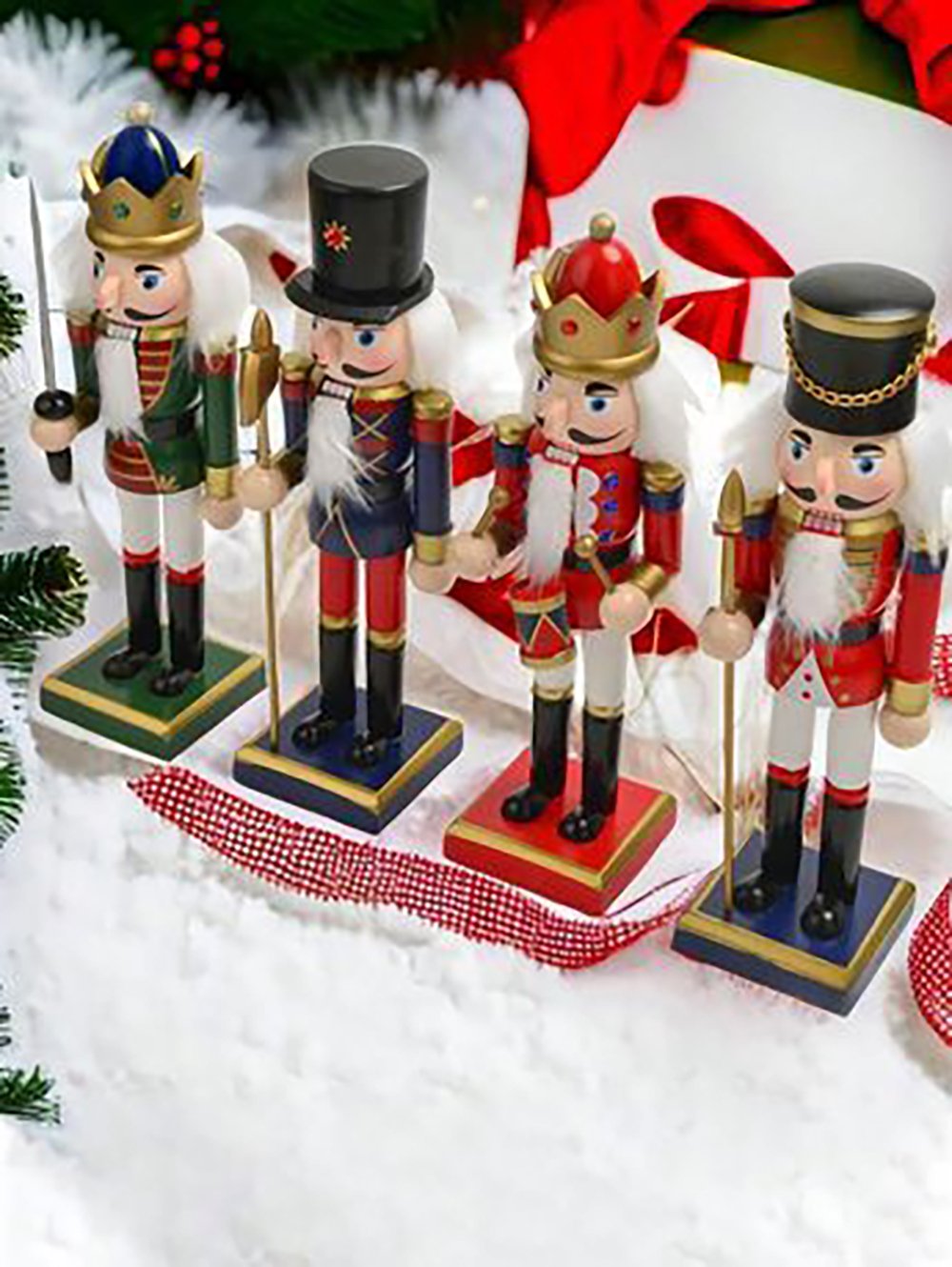 Four colorful wooden nutcracker figurines stand upright on artificial snow, each holding a staff and dressed in festive uniforms and hats. A decorated gift or Christmas ornament is visible in the background.
