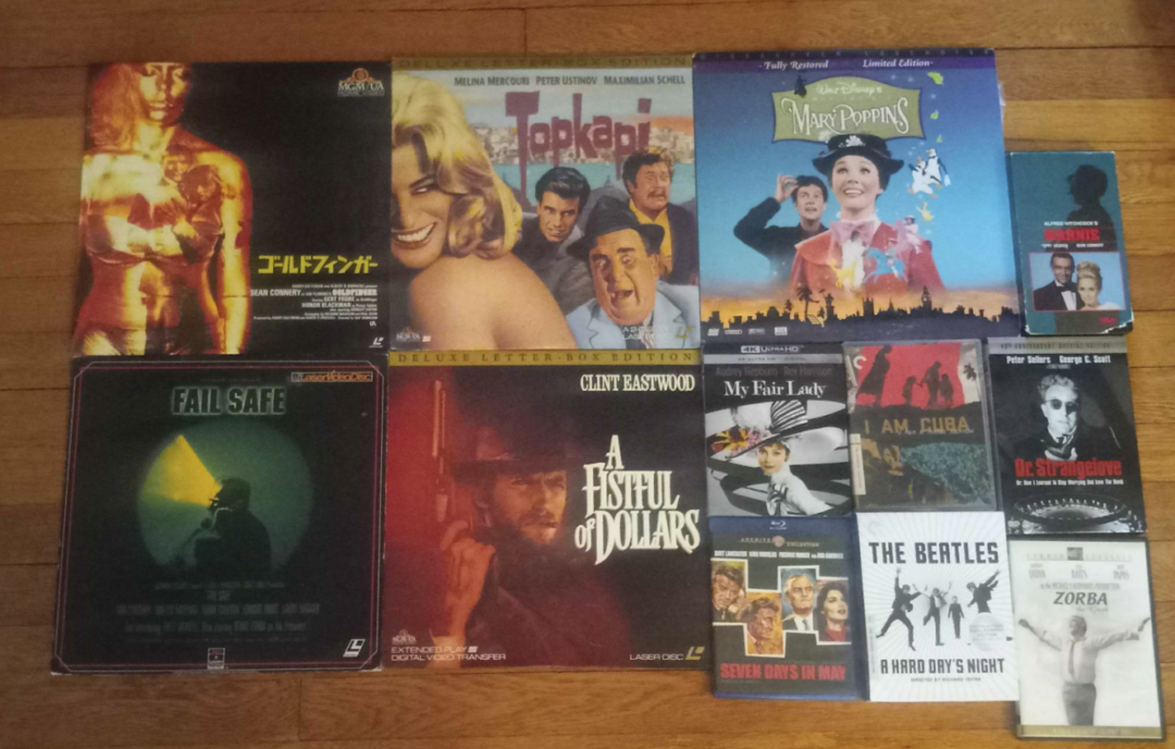 A collection of ten vintage film LaserDiscs arranged on a wooden floor, including titles like "Mary Poppins," "My Fair Lady," "A Fistful of Dollars," and "Fail Safe," with colorful and classic movie cover art.