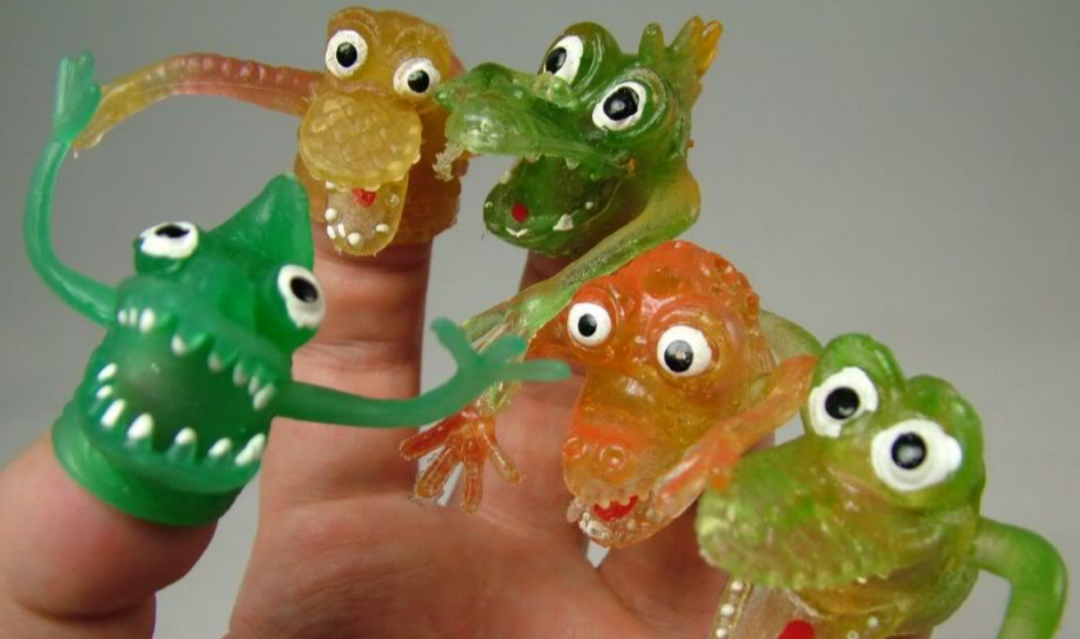 A hand with five fingers, each wearing a colorful, translucent, rubber monster finger puppet with big googly eyes and open mouths. The puppets are green, yellow, or orange.