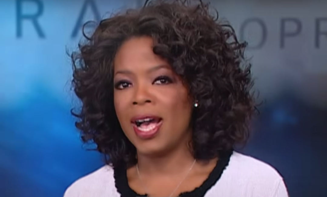 A woman with curly hair wearing a white jacket with black trim is speaking on a TV show set with a blurred blue background. The ABC logo is overlaid on the center of the image.