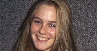 A young woman with straight, light brown hair smiles at the camera against a textured gray background. She is wearing a light-colored top.