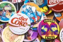 A hand holding a bunch of assorted cat Beanie Babies, each with a Ty tag, against a background of green leafy bushes.