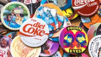 A hand holding a bunch of assorted cat Beanie Babies, each with a Ty tag, against a background of green leafy bushes.