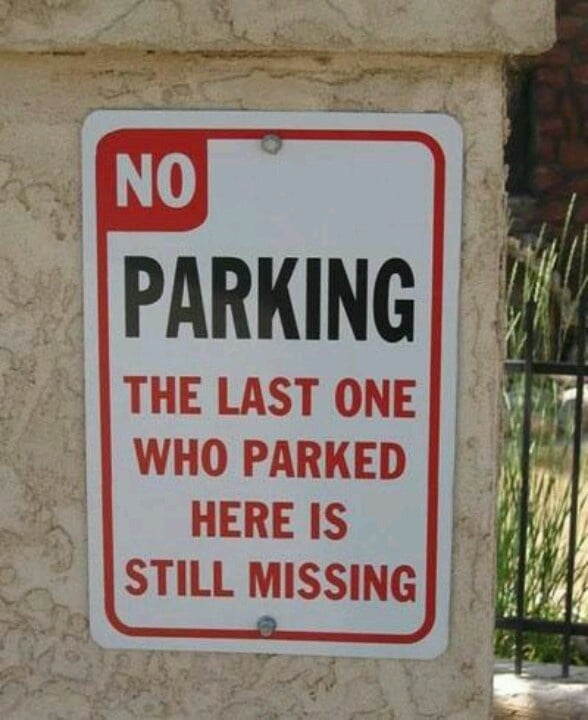 A sign on a stucco wall reads: "NO PARKING. THE LAST ONE WHO PARKED HERE IS STILL MISSING" in black and red text.