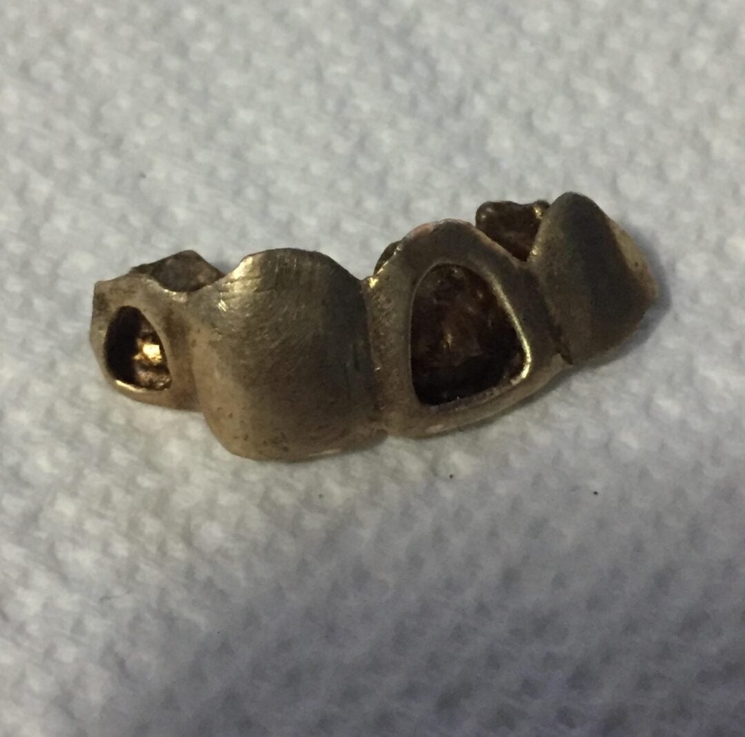 Two young men in vintage clothing are near a classic car; one is seated on a motorcycle and smiling, while the other stands beside him in a leather jacket. The scene appears to be from the mid-20th century.