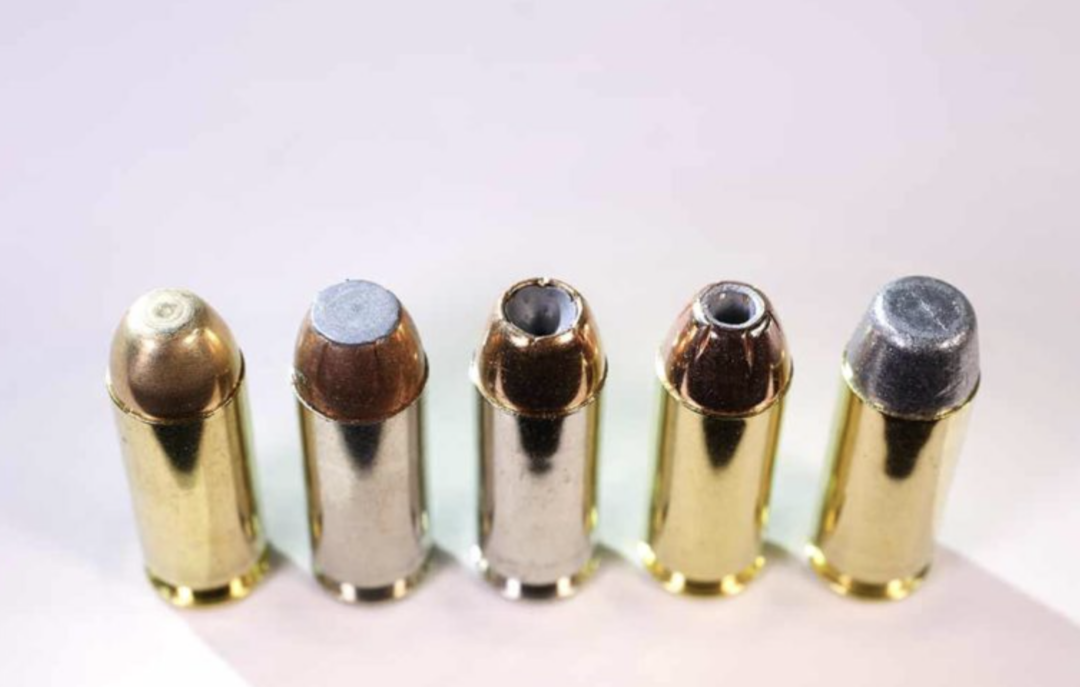 Five different types of handgun ammunition cartridges are lined up side by side on a light surface, each with a distinct bullet tip design and coloring.