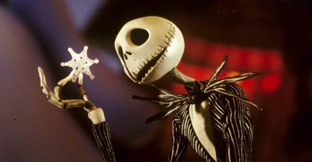 A thin skeleton character in a pinstriped suit holds a snowflake and looks at it with curiosity. The background is blurred with warm, reddish tones.