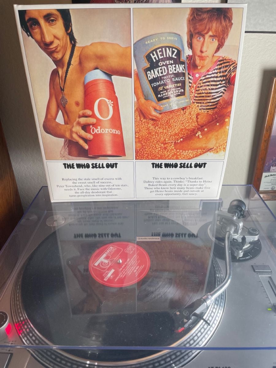 A vinyl record of "The Who Sell Out" is playing on a turntable. The album cover shows two men, one holding a large Odorono deodorant bottle, and the other with a can of Heinz baked beans spilling onto himself.