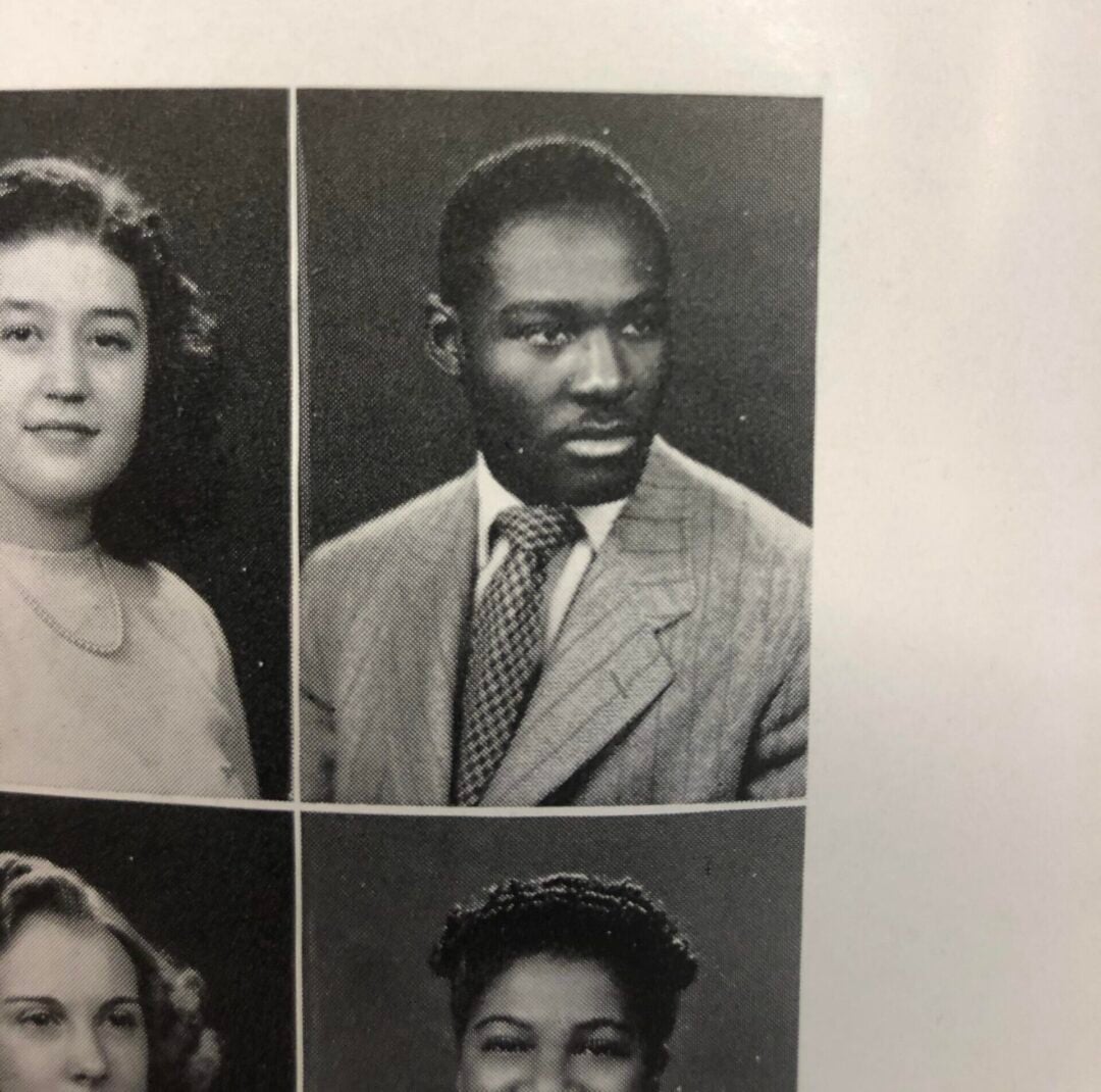 Black and white yearbook photo of a young man in a light-colored suit and tie, looking slightly to the side. He has short hair and a serious expression. Part of three other portraits are visible around him.