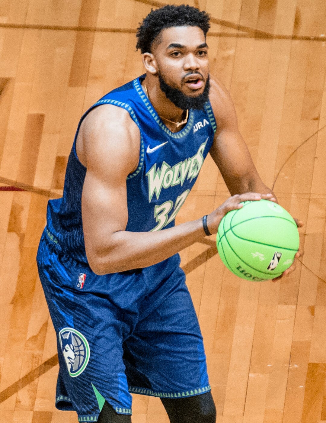 A basketball player in a blue "Wolves" jersey prepares to shoot a neon green basketball on a wooden court.