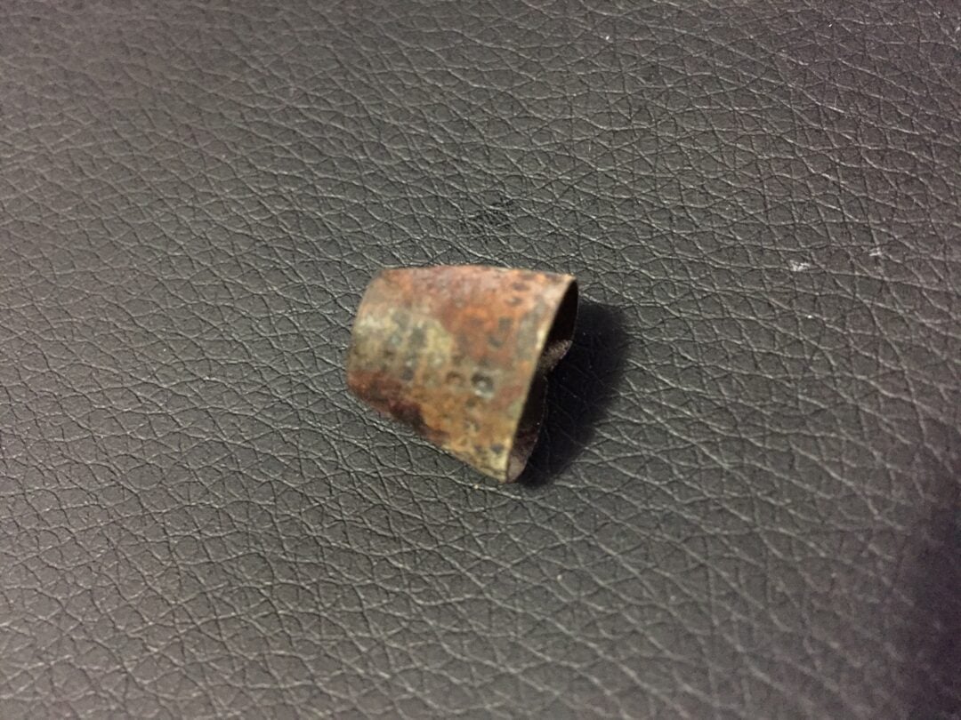 A small, rusted metal object with a cylindrical shape and an uneven edge rests on a textured black surface.