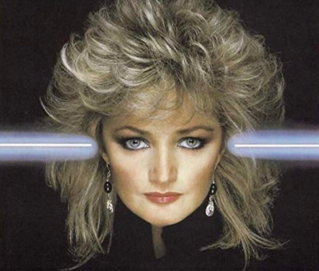 Album cover featuring Bonnie Tyler’s face with dramatic makeup and voluminous blond hair. Two bright light beams cross horizontally at her eyes. Text above reads: “Bonnie Tyler - Faster Than The Speed Of Night.”
