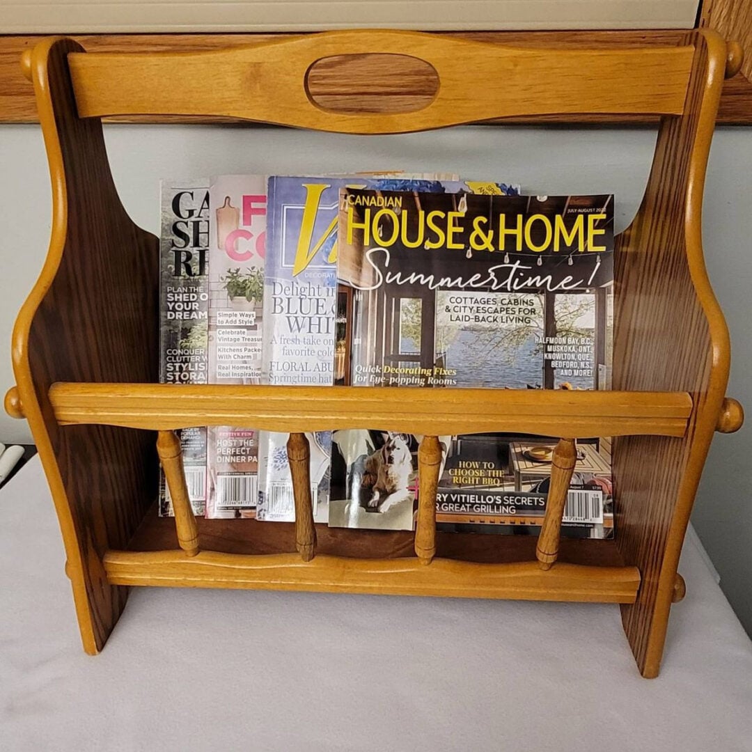 A wooden magazine rack holding various magazines, including issues of Canadian House & Home and other home and fashion publications, placed on a light-colored surface near a window.