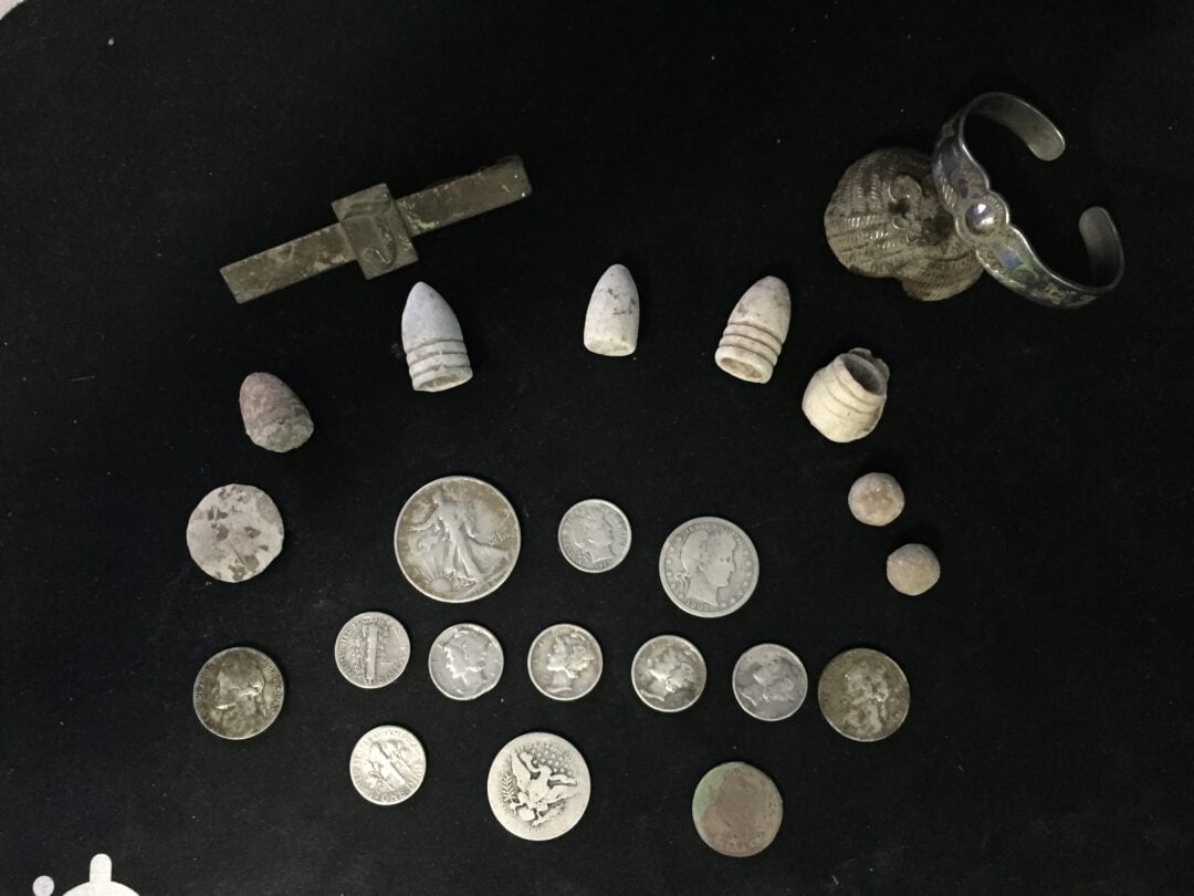 A young woman ties a scarf around a smiling young man's neck as another girl looks on. The man wears a varsity jacket with the letter "T" and the number "46." They all appear happy and are outdoors.