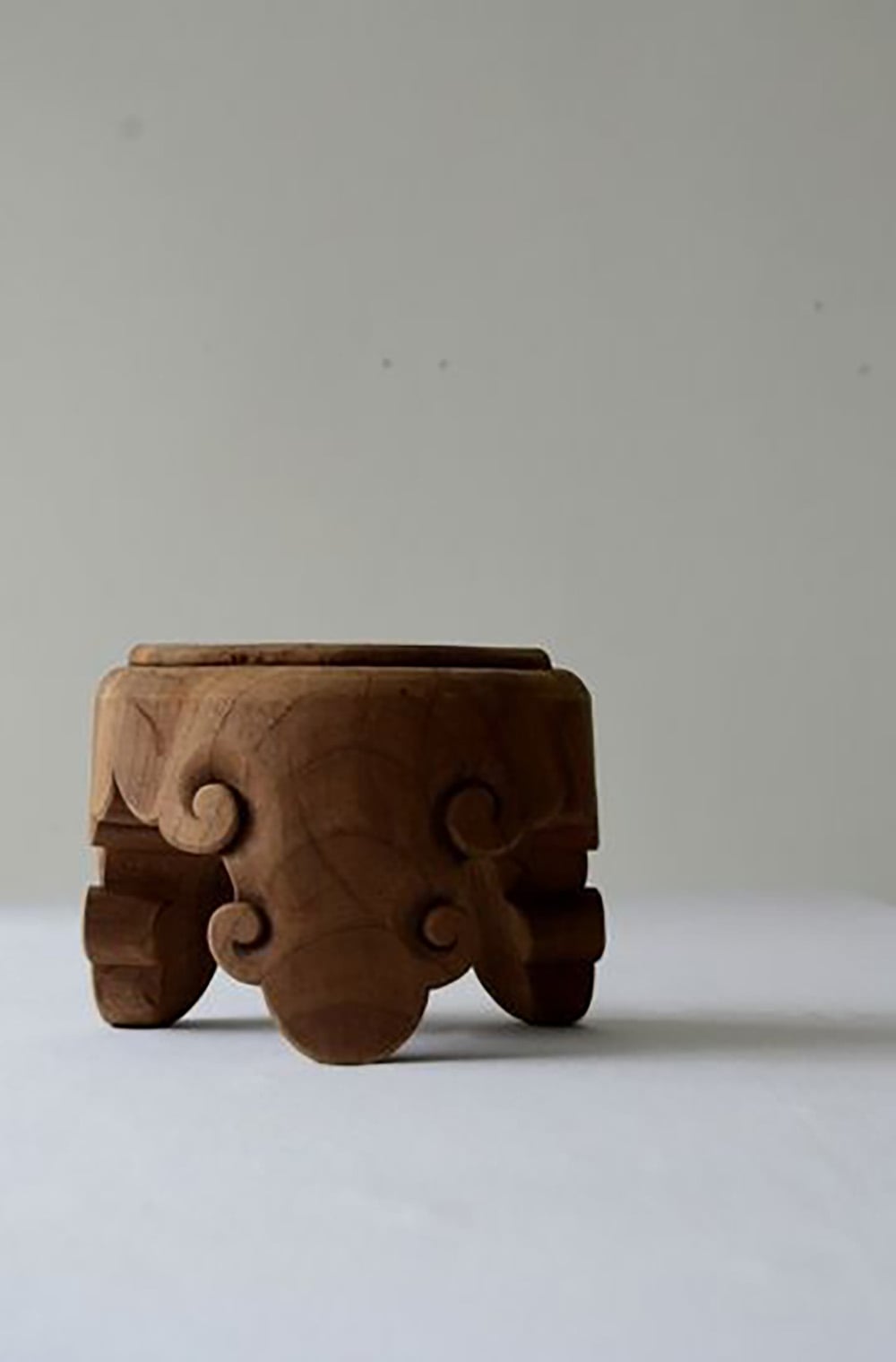 A small, carved wooden bowl with ornate scrollwork and three short legs, placed on a plain white surface against a light gray background.