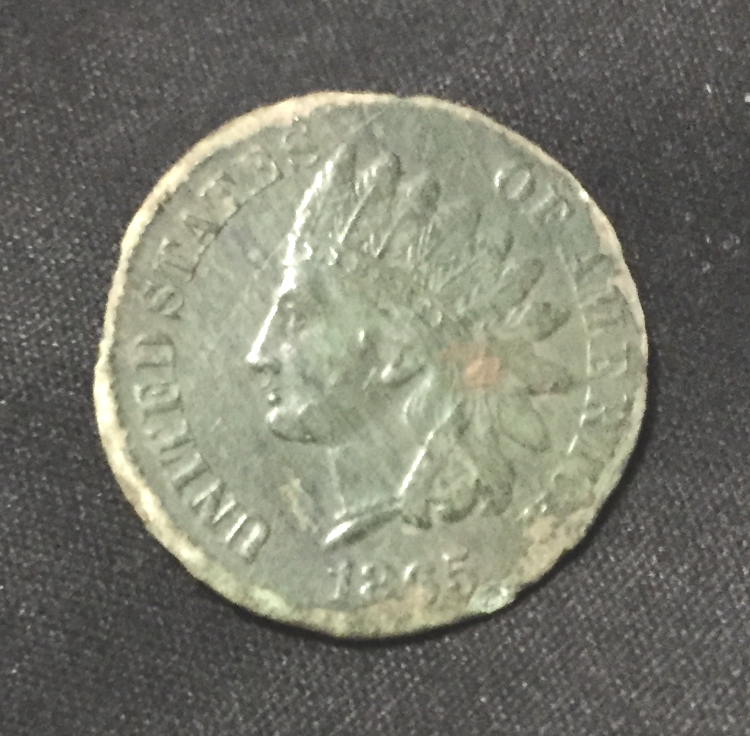 A worn 1895 United States Indian Head cent coin is displayed on a black fabric background, showing the left-facing profile of a person wearing a Native American headdress.
