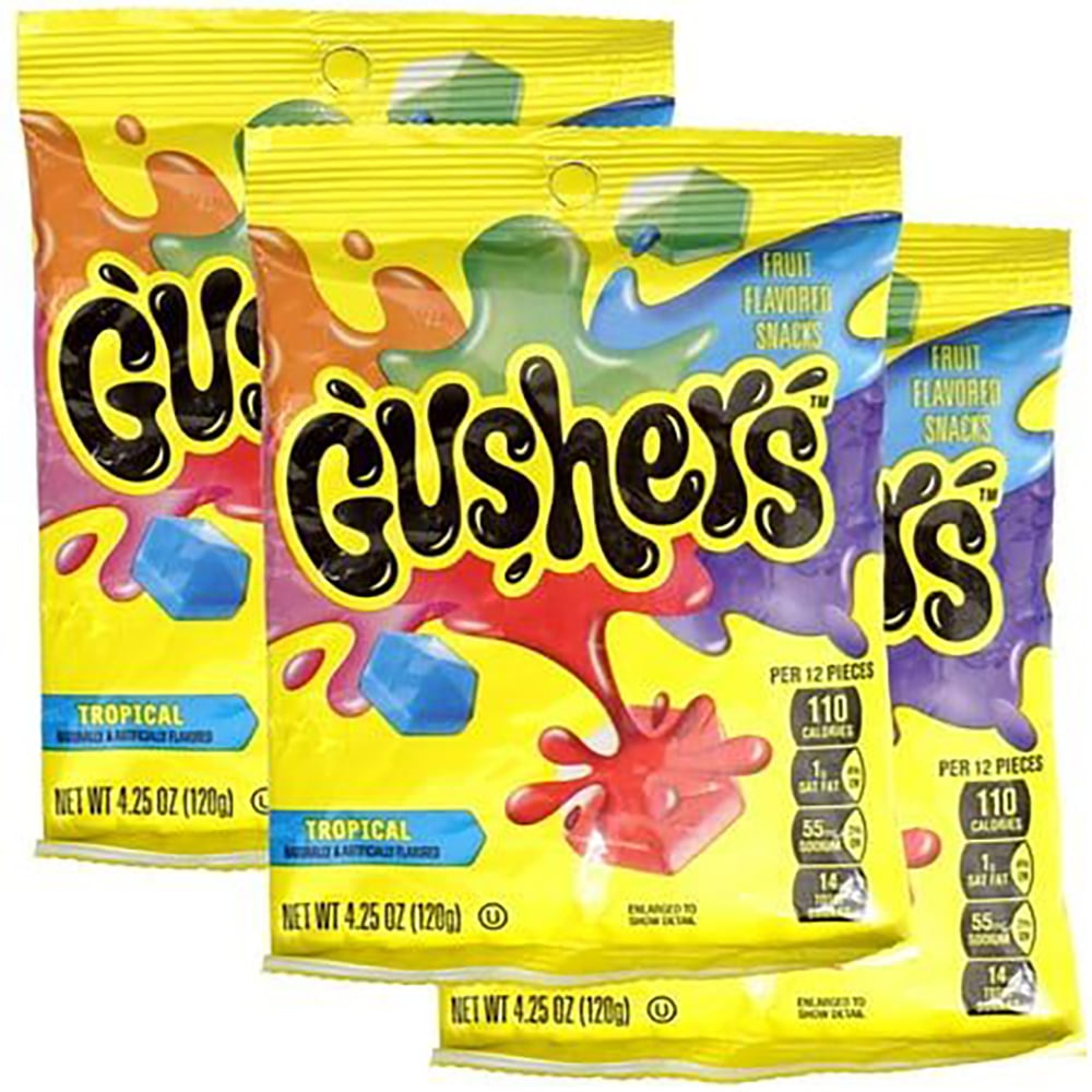 Three brightly colored bags of Tropical Gushers fruit-flavored snacks are shown, featuring splashes of red, blue, and green on yellow packaging. Each bag is 4.25 oz and displays nutritional information.