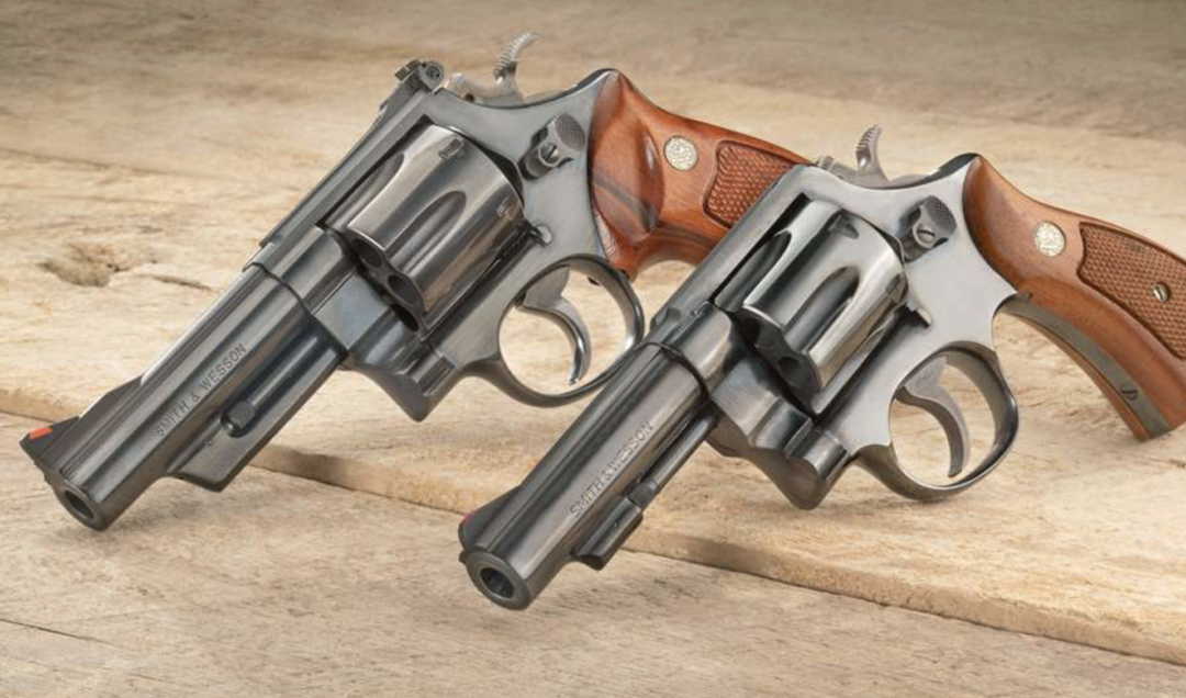 Two silver revolvers with wooden grips are placed side by side on a light wooden surface, both angled slightly to the left.