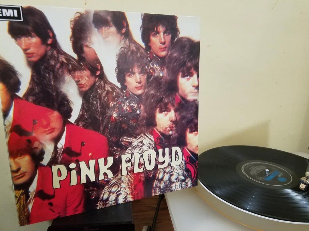 A vinyl record plays next to the album cover of Pink Floyd’s "The Piper at the Gates of Dawn," featuring multiple images of the band members in colorful, psychedelic clothing.