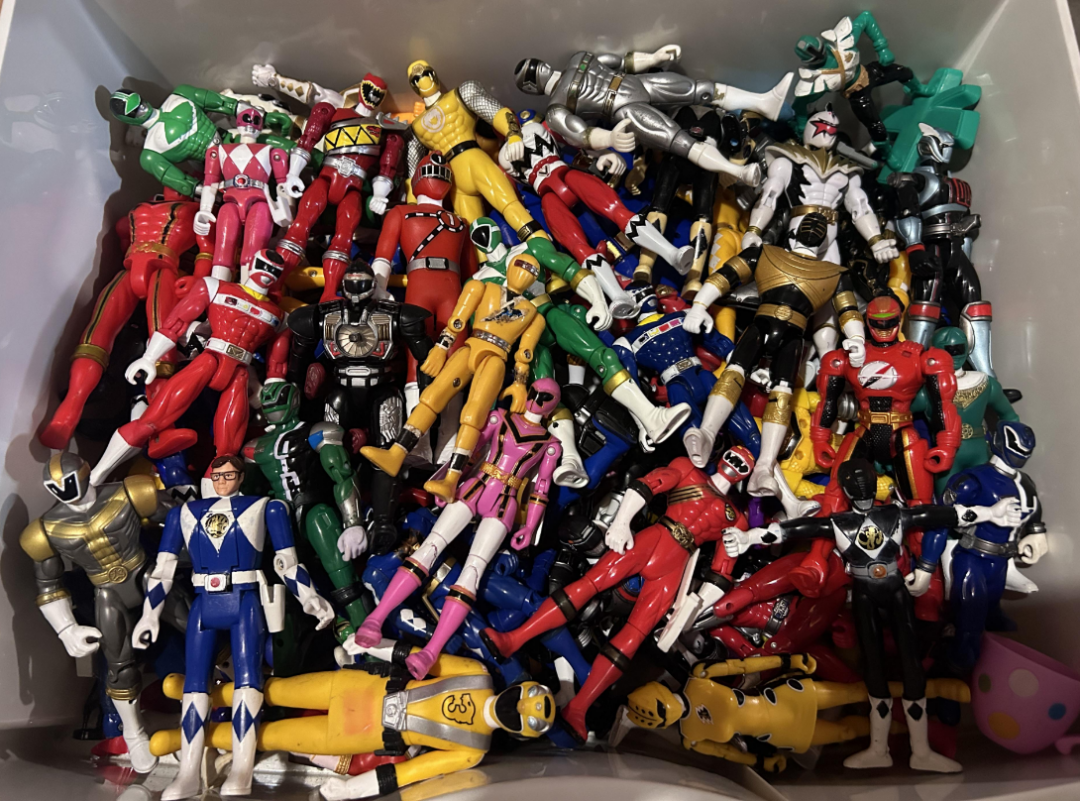 A box filled with a large collection of colorful Power Rangers action figures, including red, yellow, green, blue, pink, and black suits, arranged in various positions and overlapping each other.