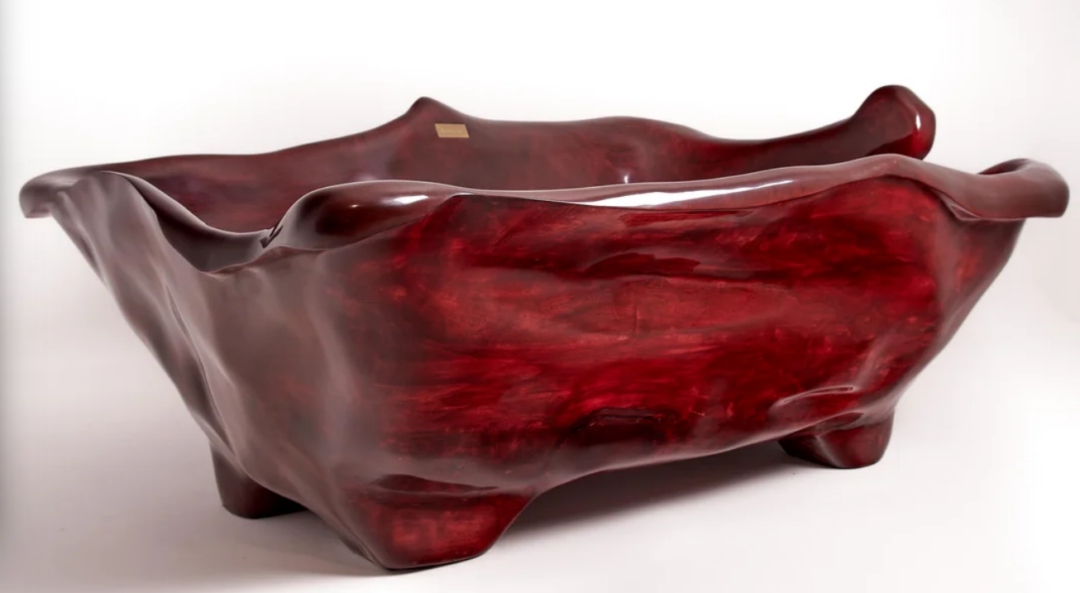 A sculpted, deep red, glossy bathtub with an organic, wavy shape and irregular edges, set against a plain white background.