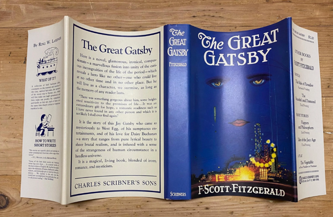 A hardcover copy of "The Great Gatsby" by F. Scott Fitzgerald, with its dust jacket open to show the front, spine, and back. The iconic blue cover features eyes and lips above glowing city lights.