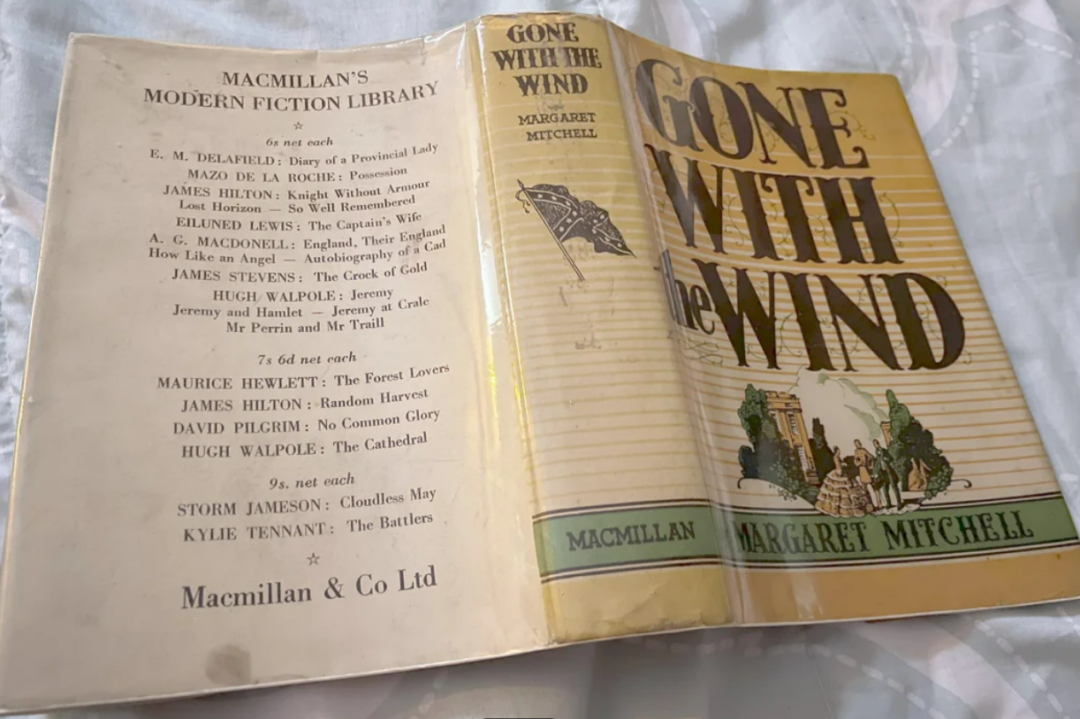 A worn hardcover copy of "Gone With the Wind" by Margaret Mitchell, published by Macmillan, rests open on a surface, showing the book’s yellow dust jacket and a list of modern fiction titles inside.