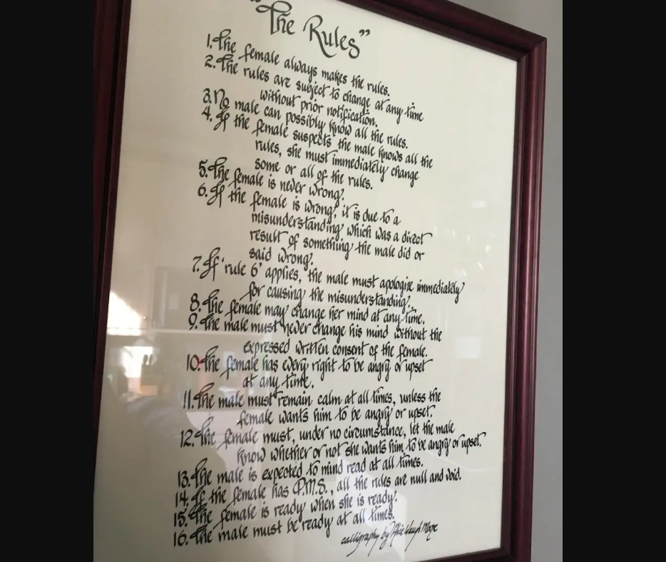 A framed document titled "The Rules" lists humorous, handwritten relationship rules, mostly stating that the female makes or changes the rules and the male must obey them. The text is in cursive with a reflective glass surface.