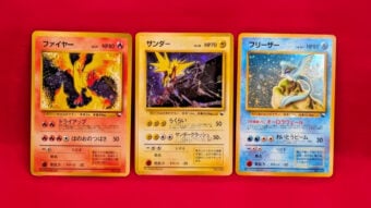 Three vintage Japanese Pok&eacute;mon cards&mdash;Moltres, Zapdos, and Articuno&mdash;are displayed side by side against a bright red background. Each card features its respective legendary bird with corresponding colors.