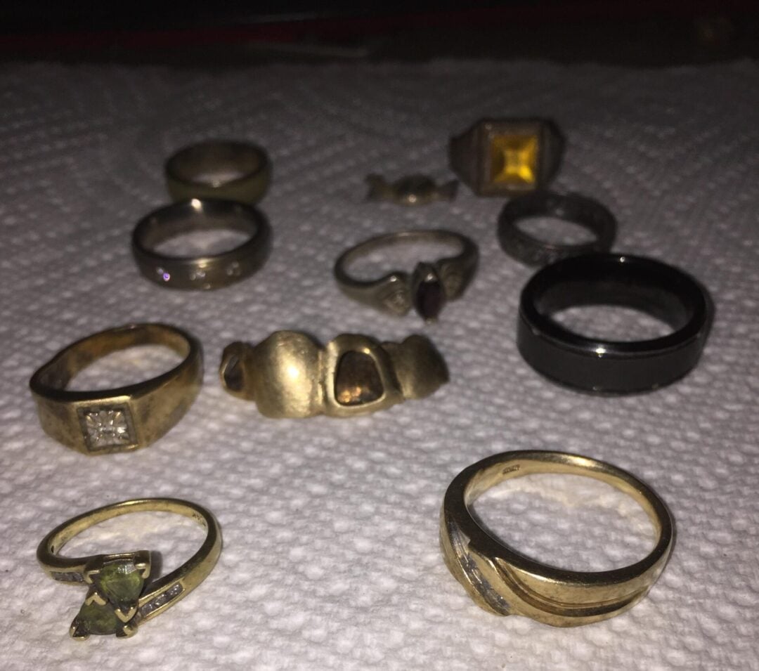 Several gold and silver rings with various designs and stones are arranged on a textured white paper towel. The rings vary in size, shape, and style, and some feature gemstones or unique engravings.
