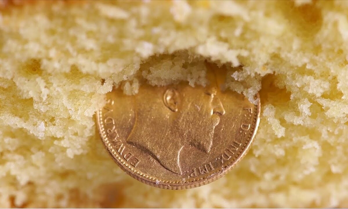 A gold coin partially embedded in the crumbly center of a yellow sponge cake.