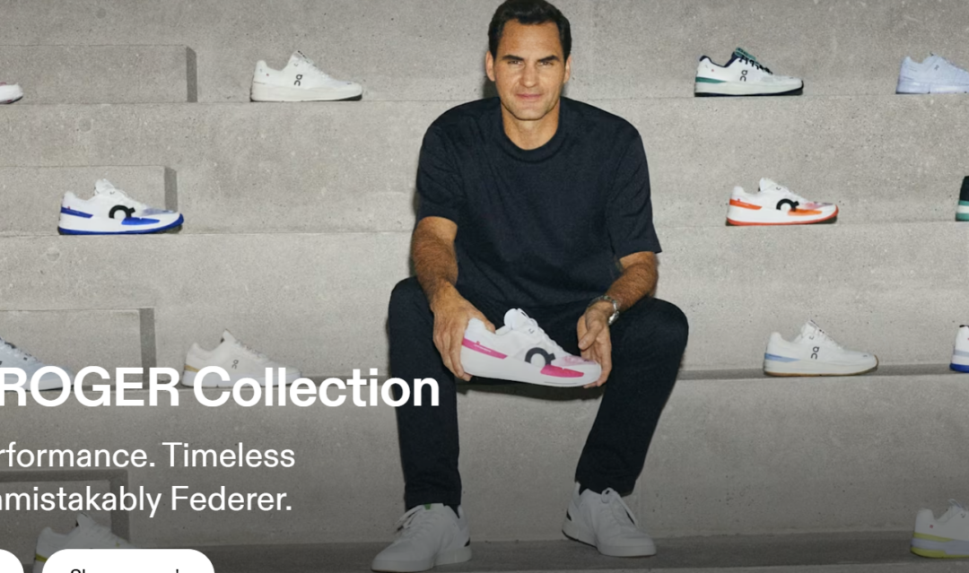 A man in a black t-shirt and pants sits on gray steps, holding a white sneaker with pink accents. Several pairs of sneakers in different colors are displayed on the steps around him.