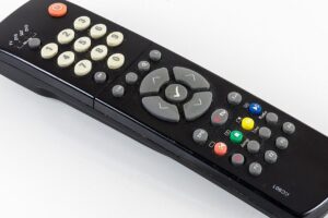 A black TV remote control with white number buttons, gray direction arrows, and several colored buttons (red, green, yellow, blue) on a white surface.