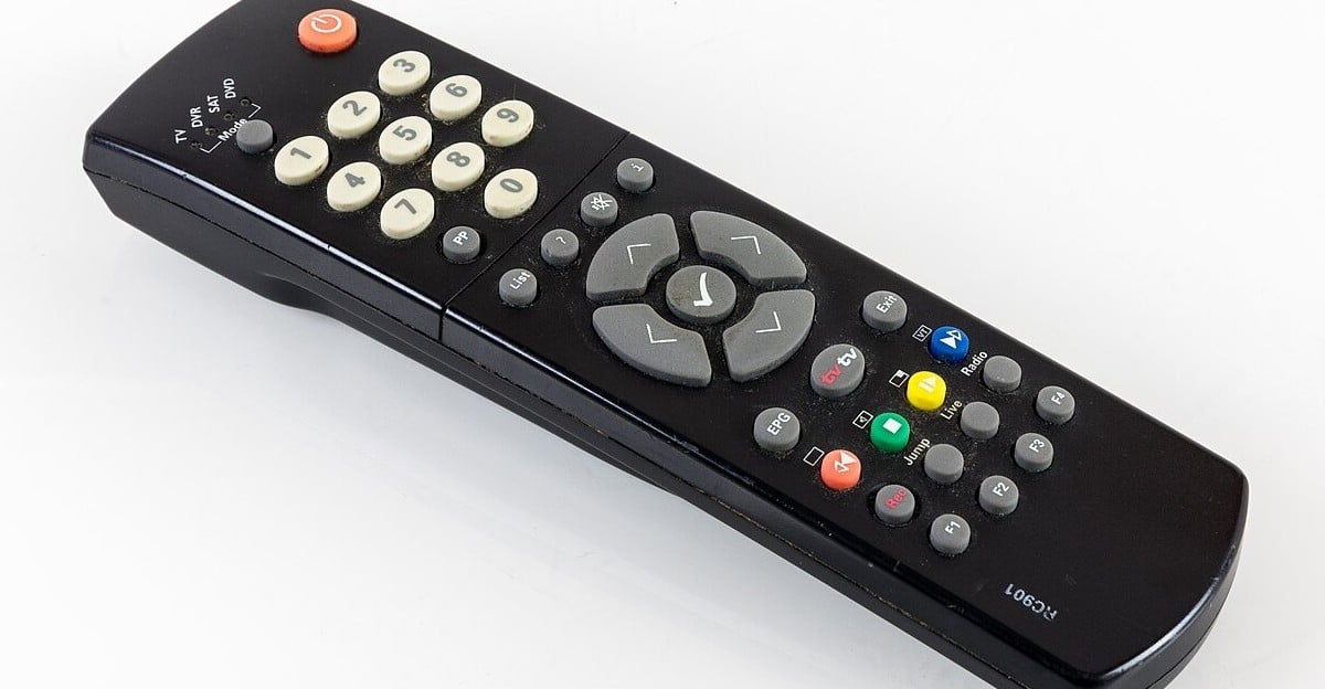 A black TV remote control with white number buttons, gray direction arrows, and several colored buttons (red, green, yellow, blue) on a white surface.