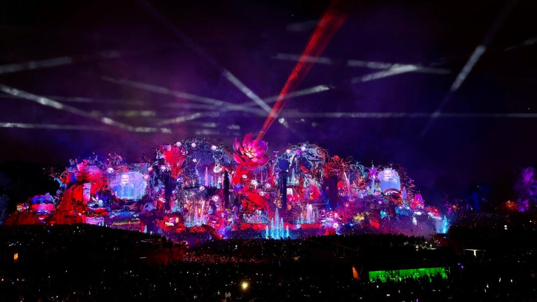 A distant view of Angkor Wat temple surrounded by lush green trees, with its iconic towers rising above the forest under a hazy sky.