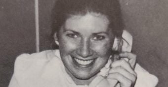 A woman smiling and holding a corded telephone receiver to her ear. The image is in black and white.