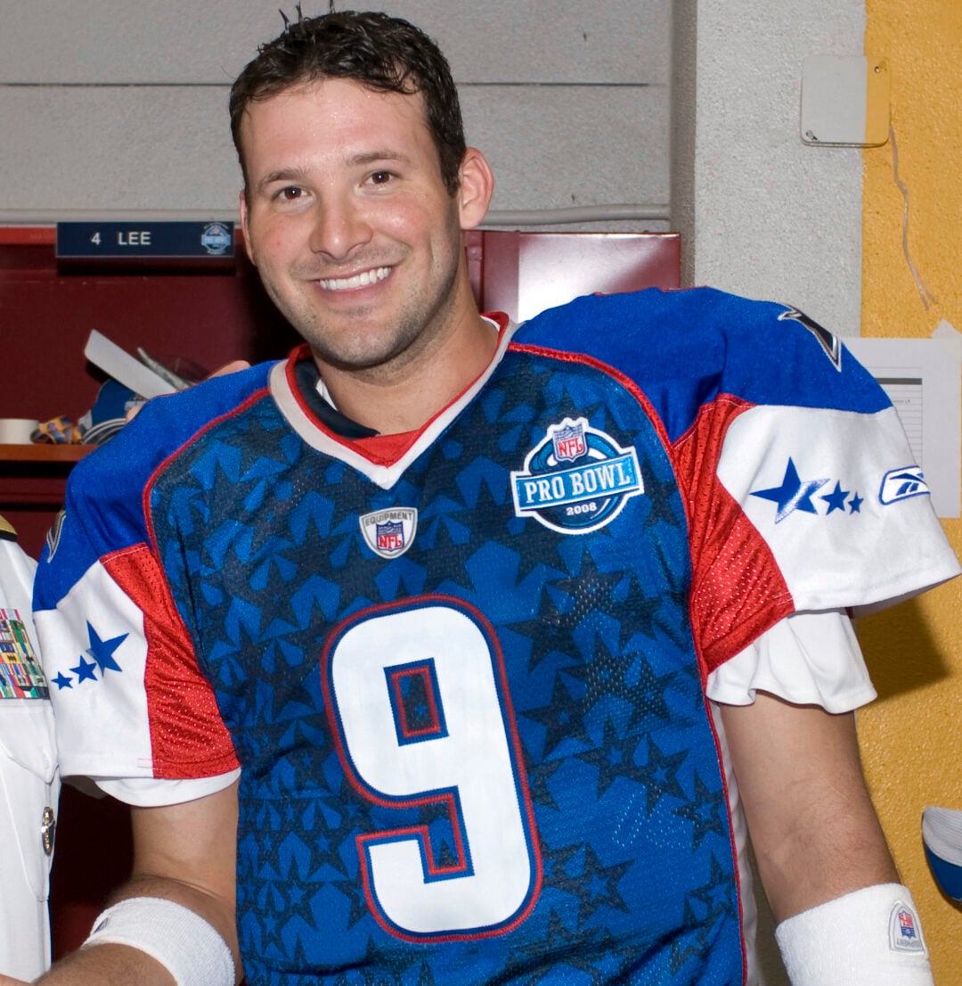 A smiling football player wearing a blue Pro Bowl jersey with the number 9, standing indoors with his left arm raised at his side.