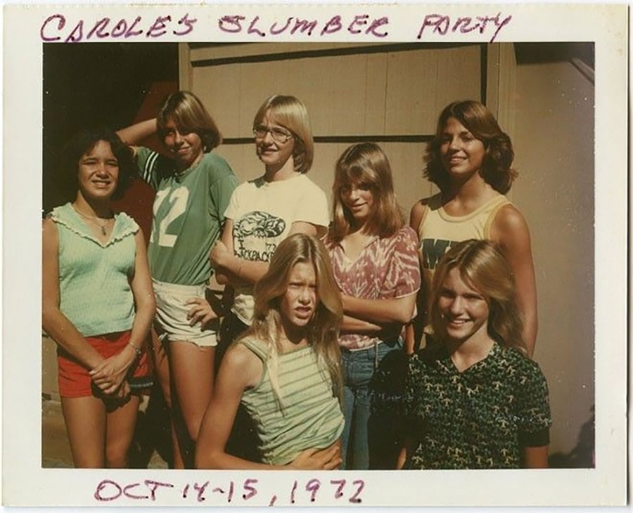 Seven smiling girls pose outside in casual 1970s clothing. Handwritten text on the photo reads, “CAROLE’S SLUMBER PARTY” at the top and “OCT. 14-15, 1977” at the bottom.